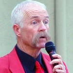 Patt Abbatt holding a microphone and wearing a red tie and jacket