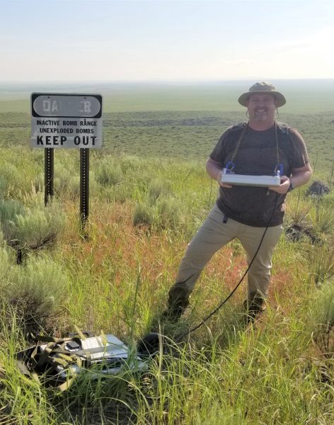 Michael Levenson standing in front of and unexploded bomb field with a GPR intena