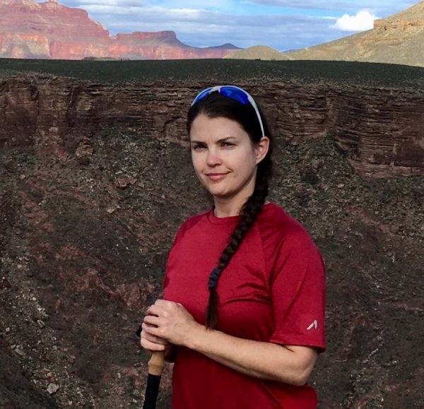 Athena Catanzaro standing on the rim of the Grand canyon in a red shirt and tan pants
