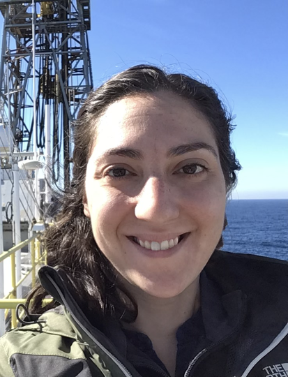 A woman with dark hair stands with the ocean and the horizon visible in the background