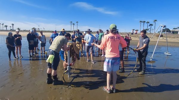 Several students work together to guide a core tube into the ground