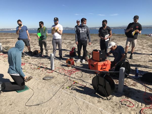 one student holding a sledgehammer in the foreground with several other students standing in the background