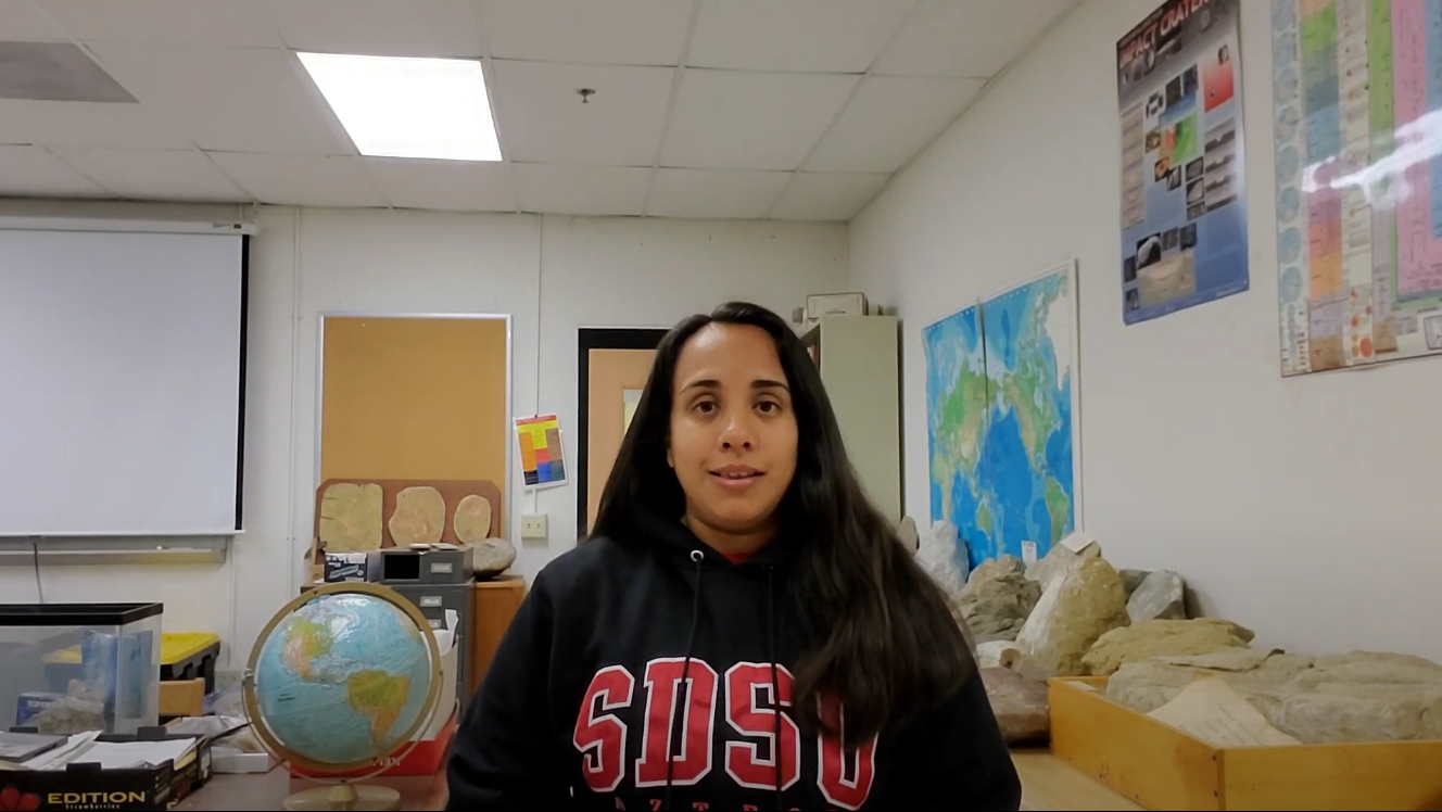 Vanessa wears an SDSU sweatshirt in a classroom displaying several rocks