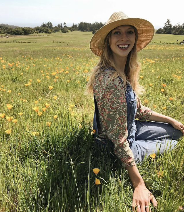 Sarah Engel wearing a straw hat sitting in a field of California Poppies