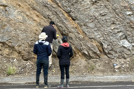 Along the side of a road in Ecuador, students gather rock samples from a diagonal rockface