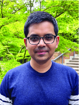 Raj Moulik wearing a blue t-shirt and black rimmed rectangle framed glasses