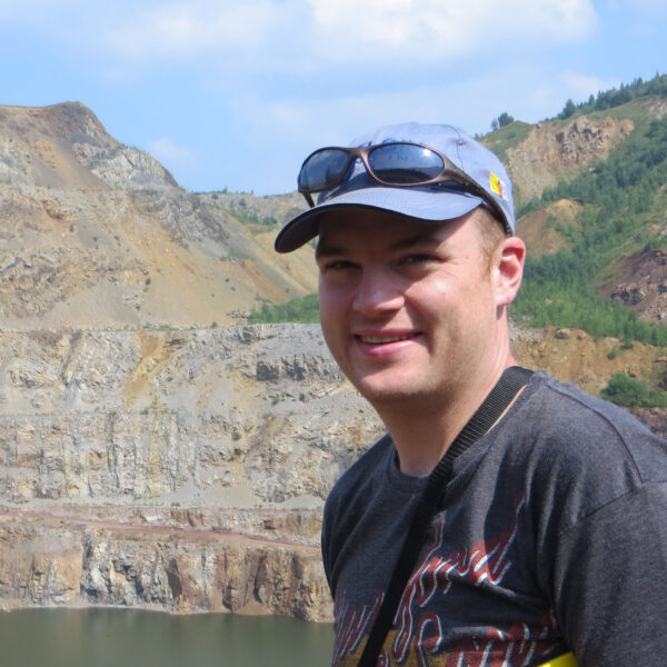 Dr. Dan Gregory wearing a blue baseball hat with sunglasses resting on the bill, a black T-shirt and smiling 